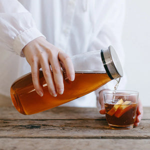 a person poured tea out of cold brew jar in glass and stainless steel by kinto into a glass